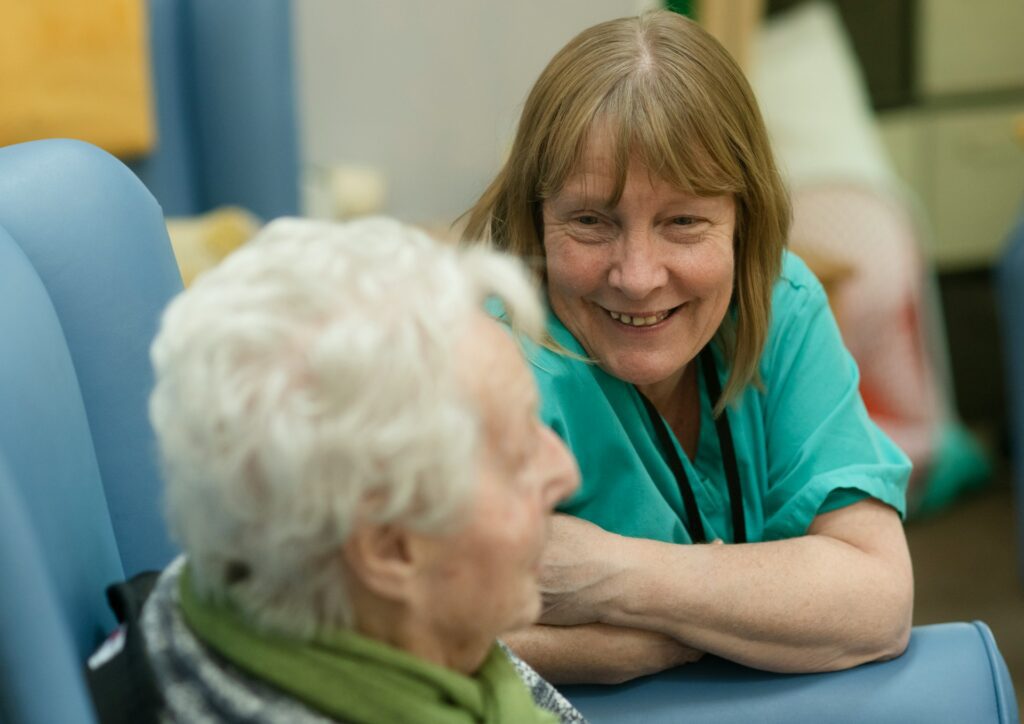 Nursing assistant in green scrubs talking with an elderly resident