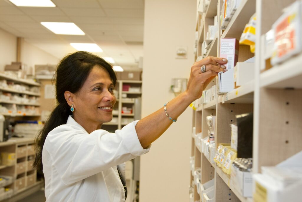 Pharmacy worker in a white coat reaching for medication on a shelf
