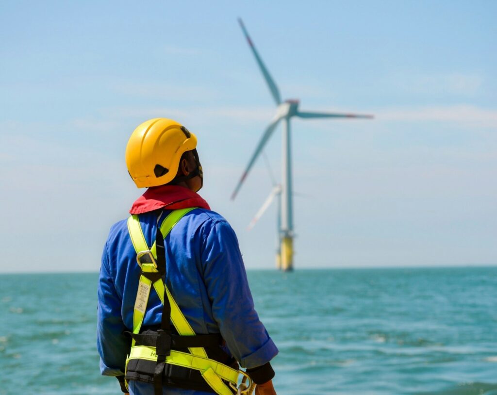 Technician in a hard hat and safety gear looking at a wind turbine